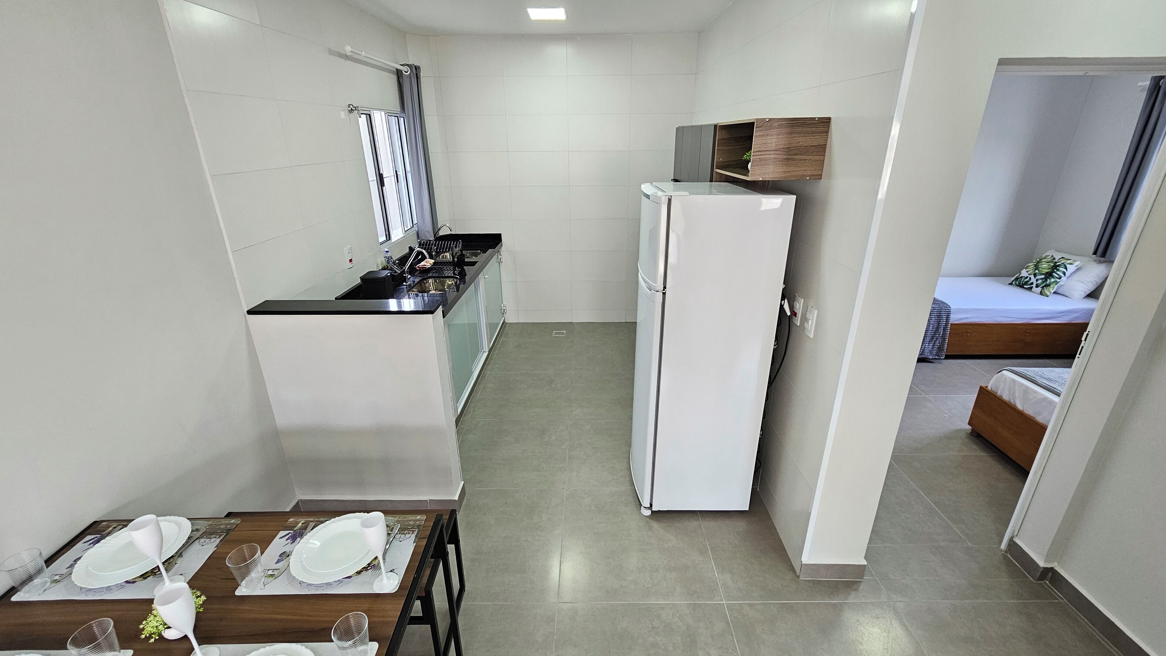 Une cuisine compacte comprenant un réfrigérateur, une table à manger avec assiettes et verres, et une petite fenêtre avec des rideaux.