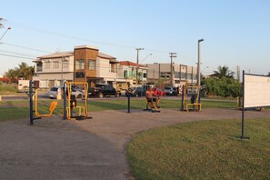 An outdoor fitness area with exercise equipment, a parking lot, and buildings in the background. - Spazio Italia Apartamentos (Ilha Comprida)
