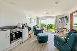 Una cocina moderna con horno empotrado, un comedor con mesa y sillas, y una sala de estar con sofá y televisor.