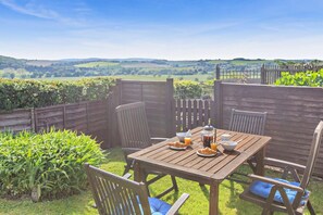 Un espace de restauration en plein air avec une table et des chaises en bois, entouré d’une clôture en bois, et offrant une vue sur un paysage pittoresque.