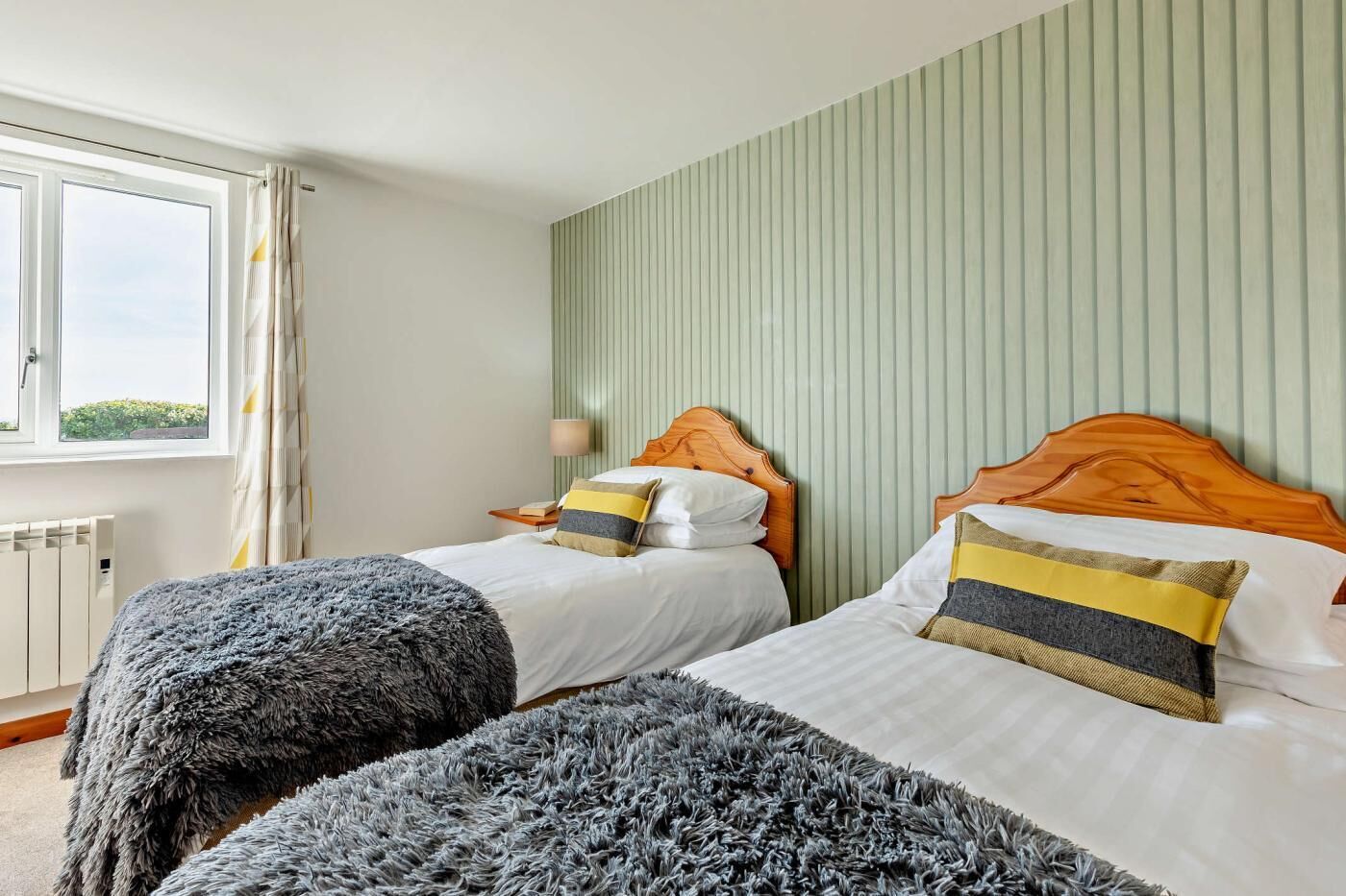 Habitación de hotel con dos camas, una ventana con cortinas, un radiador y una pared con líneas verticales.