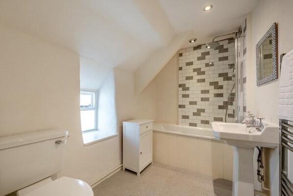 A bathroom with a toilet, a window, a shower, and a sink.