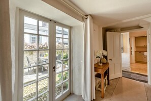 A room with a large sliding glass door leading to a patio with outdoor furniture and plants. There is a wooden side table with a vase of flowers. - 3 Bed in Appledore (oc-a29241) (Appledore)
