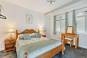 A bedroom with a wooden bed, bedside lamps, a desk with a mirror, and a framed picture on the wall. - 2 Bed in Goodleigh (oc-l29573) (Goodleigh)