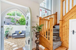 Una escalera con barandillas de madera que lleva a una plataforma, una planta en maceta y vista de un patio exterior con valla blanca y follaje.