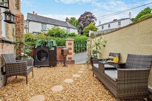 A patio with wicker furniture, a large air conditioning unit, and a decorative fountain. - 2 Bed in Goodleigh (oc-l29573) (Goodleigh)
