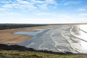 A coastal landscape with a wide sandy beach, a series of shallow pools, and gentle waves lapping onto the shore. - 3 Bed in Braunton (oc-b29581) (Braunton)