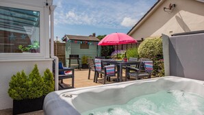 A hot tub in a backyard with a patio table and chairs, surrounded by greenery and a small shed. - 3 Bed in Braunton (oc-b29581) (Braunton)