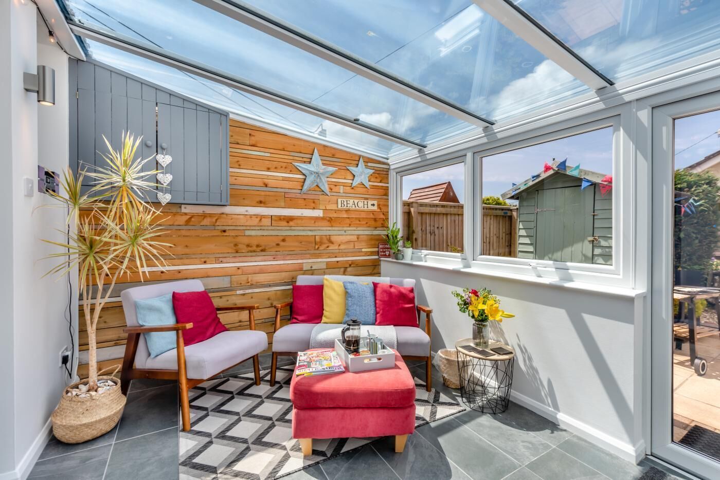 A cozy patio with a wooden wall, a cushioned seating area, and a glass enclosure.