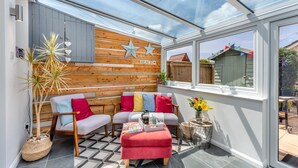 A cozy patio with a wooden wall, a cushioned seating area, and a glass enclosure. - 3 Bed in Braunton (oc-b29581) (Braunton)