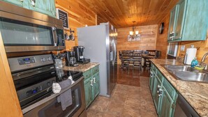 A modern kitchen with stainless steel appliances, green cabinets, and a wooden ceiling.