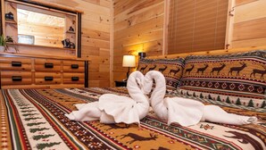 A wooden cabin room with a bed featuring a patterned blanket, a dresser with drawers, a lamp, and a mirror on the wall.