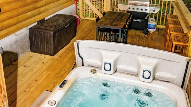 A wooden deck with a hot tub, a grill, and a TV screen.