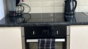 Una cocina con encimera negra, cafetera, hervidor y estufa.