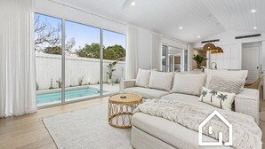 Un salon moderne doté d’un grand canapé, d’une table basse ronde en osier et offrant une vue sur une piscine grâce à de grandes baies vitrées.
