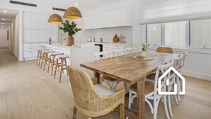 Une cuisine moderne avec des meubles blancs, une table à manger en bois, des chaises en osier et des luminaires suspendus.