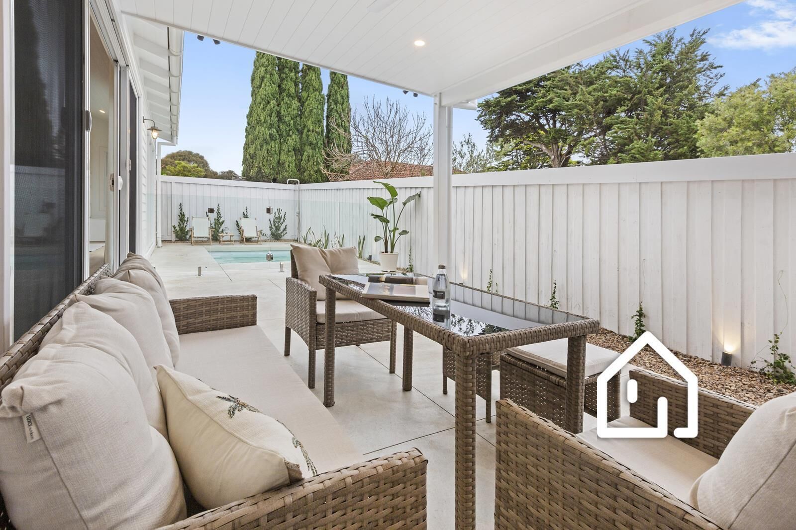An outdoor patio with wicker furniture, a pool, and a white fence.