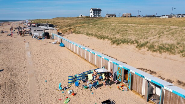 A beachside caravan park with multiple caravans and tents, a sandy beach, and a grassy dune area in the background.