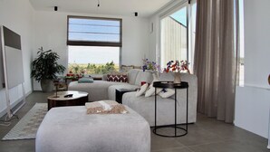 A modern living room with a large window, a sofa, a coffee table, and a potted plant.