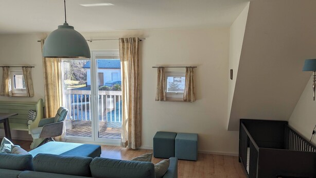 Un salon avec un canapé, une table et une chaise. Il y a un balcon avec une balustrade et des rideaux.