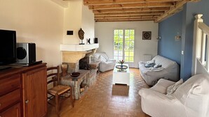 Un salon spacieux doté d’une cheminée, de poutres apparentes, d’un canapé blanc et d’un téléviseur posé sur un meuble en bois.