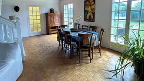 Un espace repas comprenant une table et des chaises en bois, un lustre et de grandes fenêtres donnant sur l’extérieur.