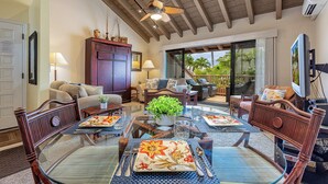 A spacious living room with a high ceiling, a dining area with a glass table, and a view of the outdoors through large sliding glass doors. - Maui Kamaole M207 Kihei condo w/ pool, hot tub and sunset lanai, summer deal (Kihei)