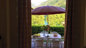 Ein Tisch mit einem violetten Sonnenschirm, weißen Stühlen und einer Blumenvase.