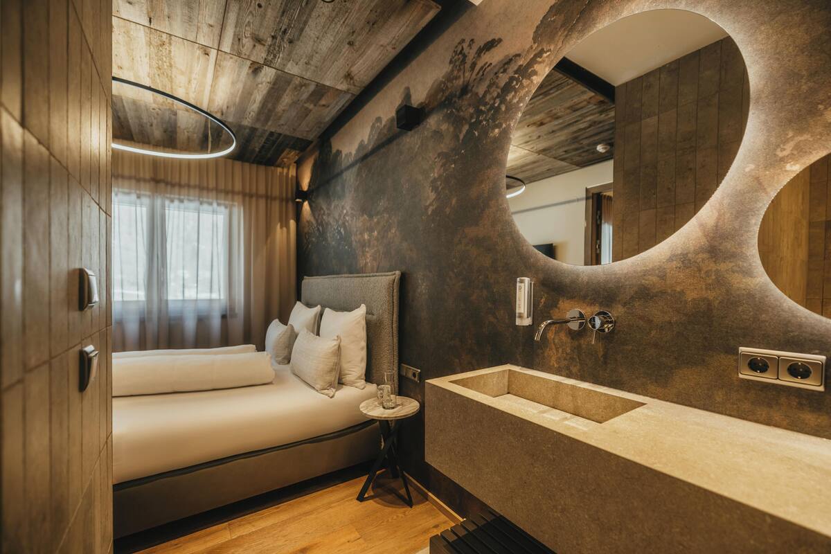 Un dormitorio moderno con una cama grande, un espejo redondo y una bañera empotrada.