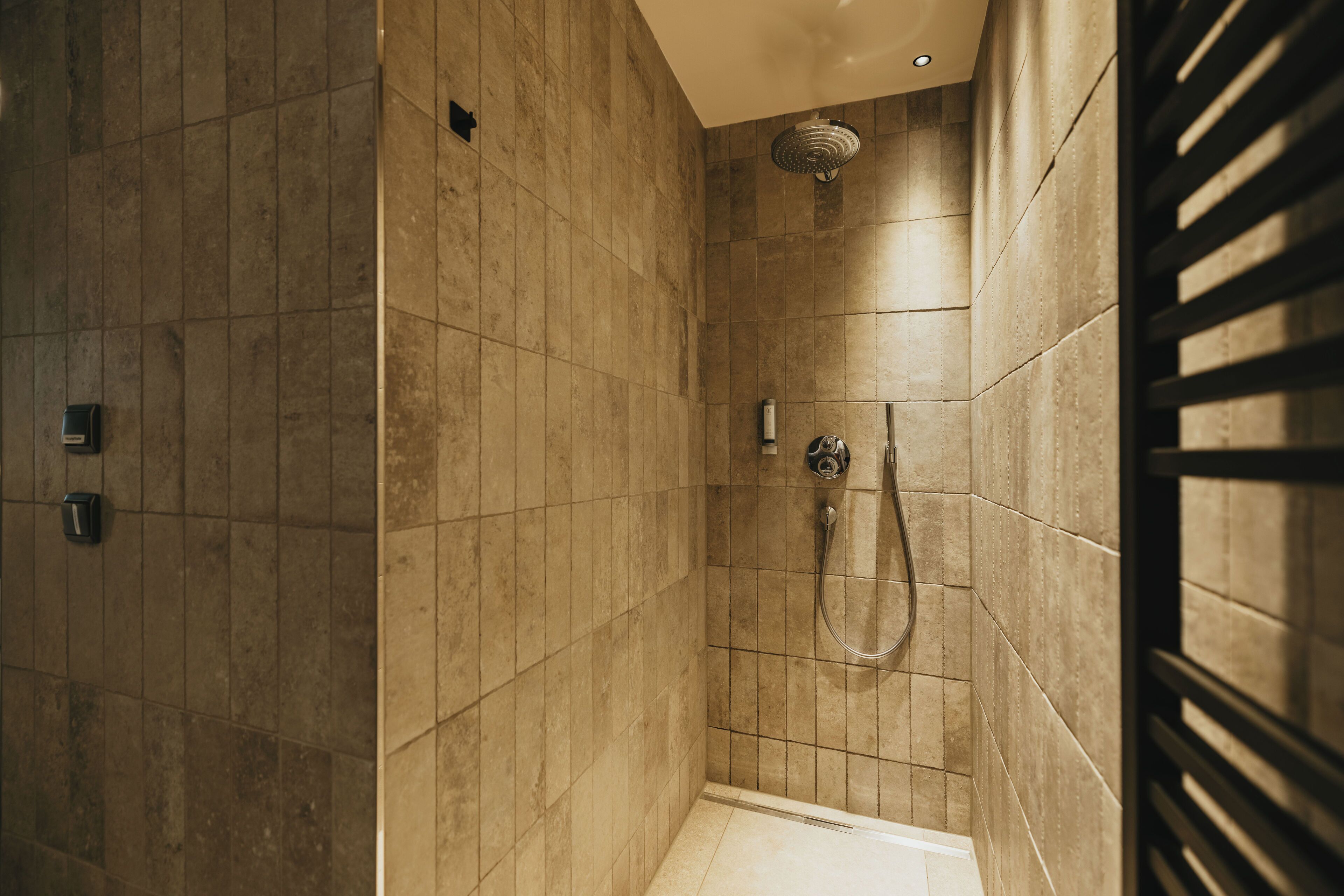 A modern shower with a handheld showerhead and a wall-mounted faucet.