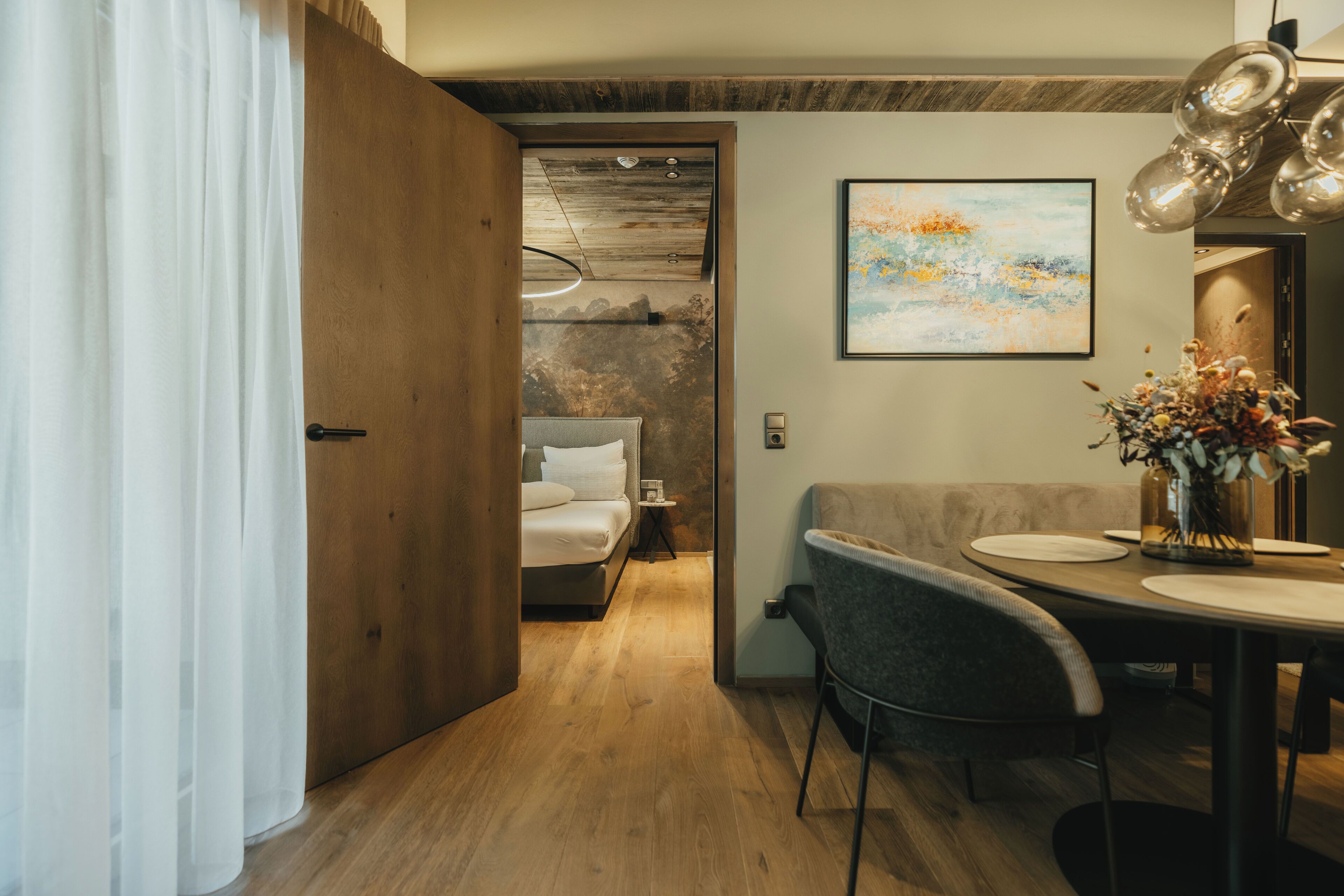 Un interior moderno con piso de madera, un comedor con mesa y sillas, un sofá y una cama con cabecera.
