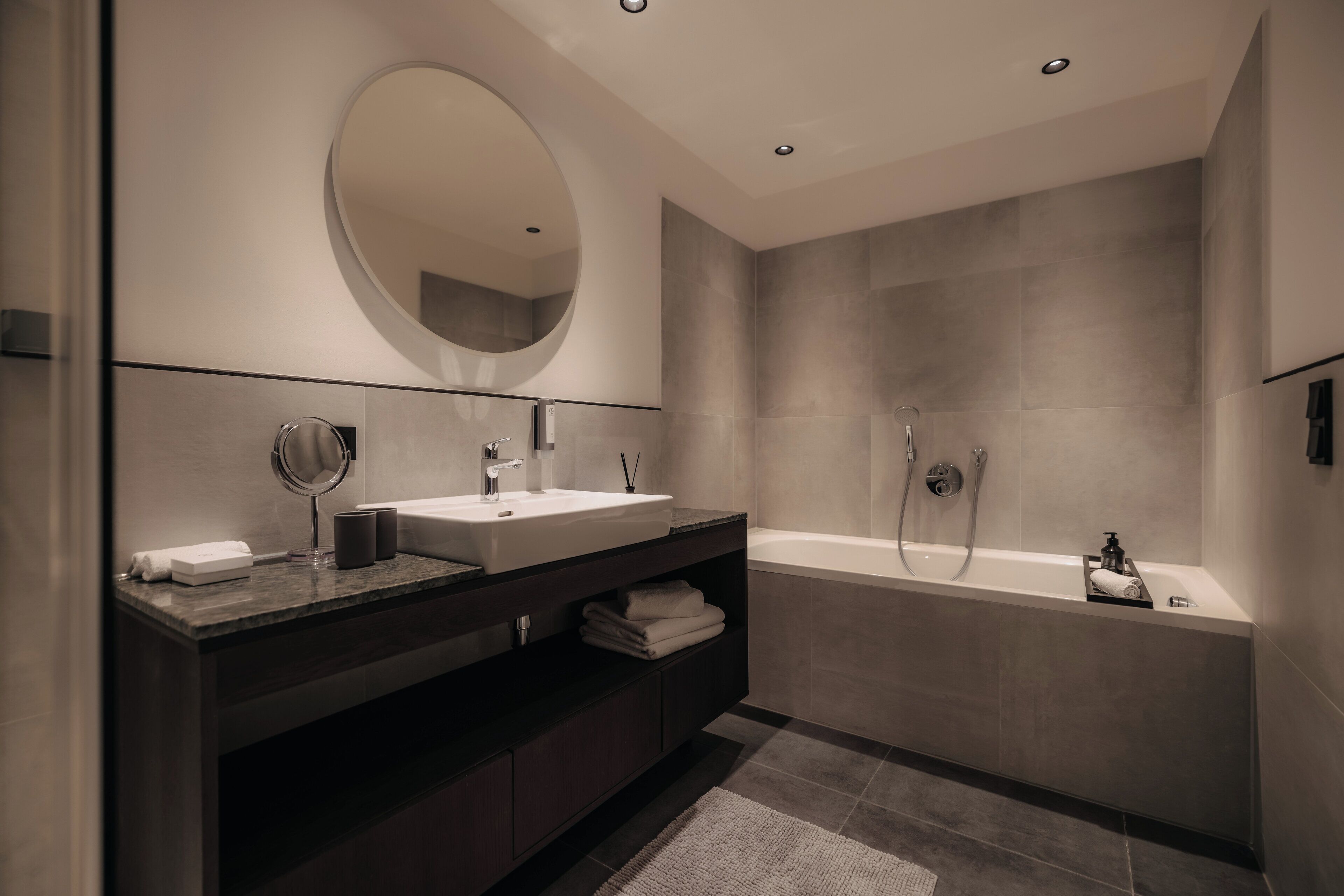 Un baño moderno con un espejo grande, dos lavamanos, una bañera y un mueble de tocador de madera oscura.