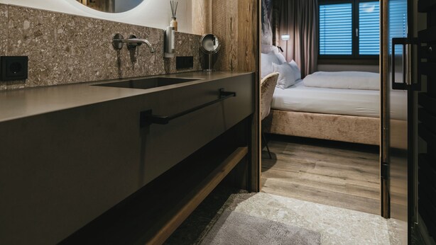Een moderne badkamer met een grote spiegel, een granieten aanrechtblad en een houten wastafelmeubel.