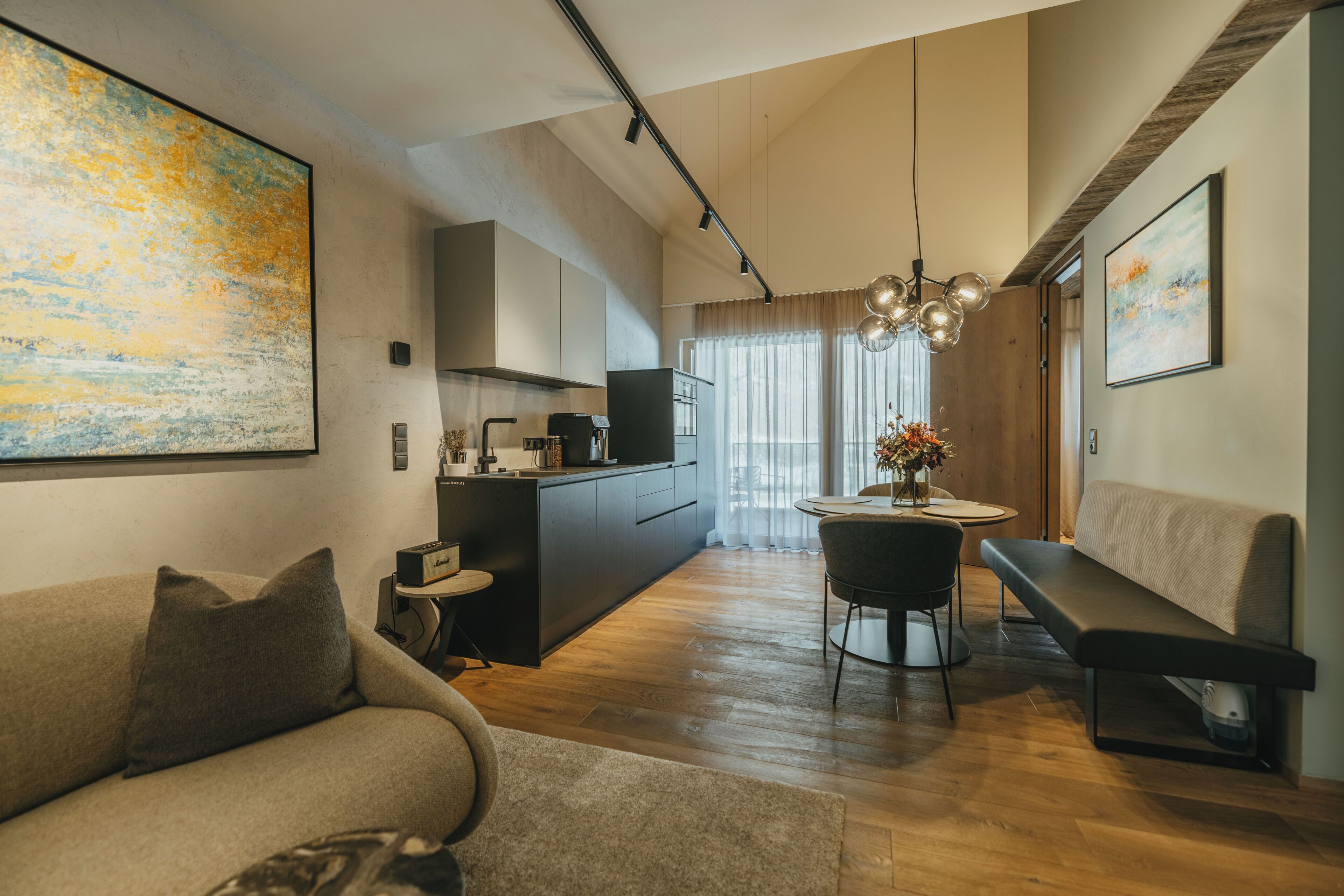 Ein modernes Wohnzimmer mit einer Couch, einem Esstisch mit Stühlen, einer Bank und einem Küchenbereich im Hintergrund.