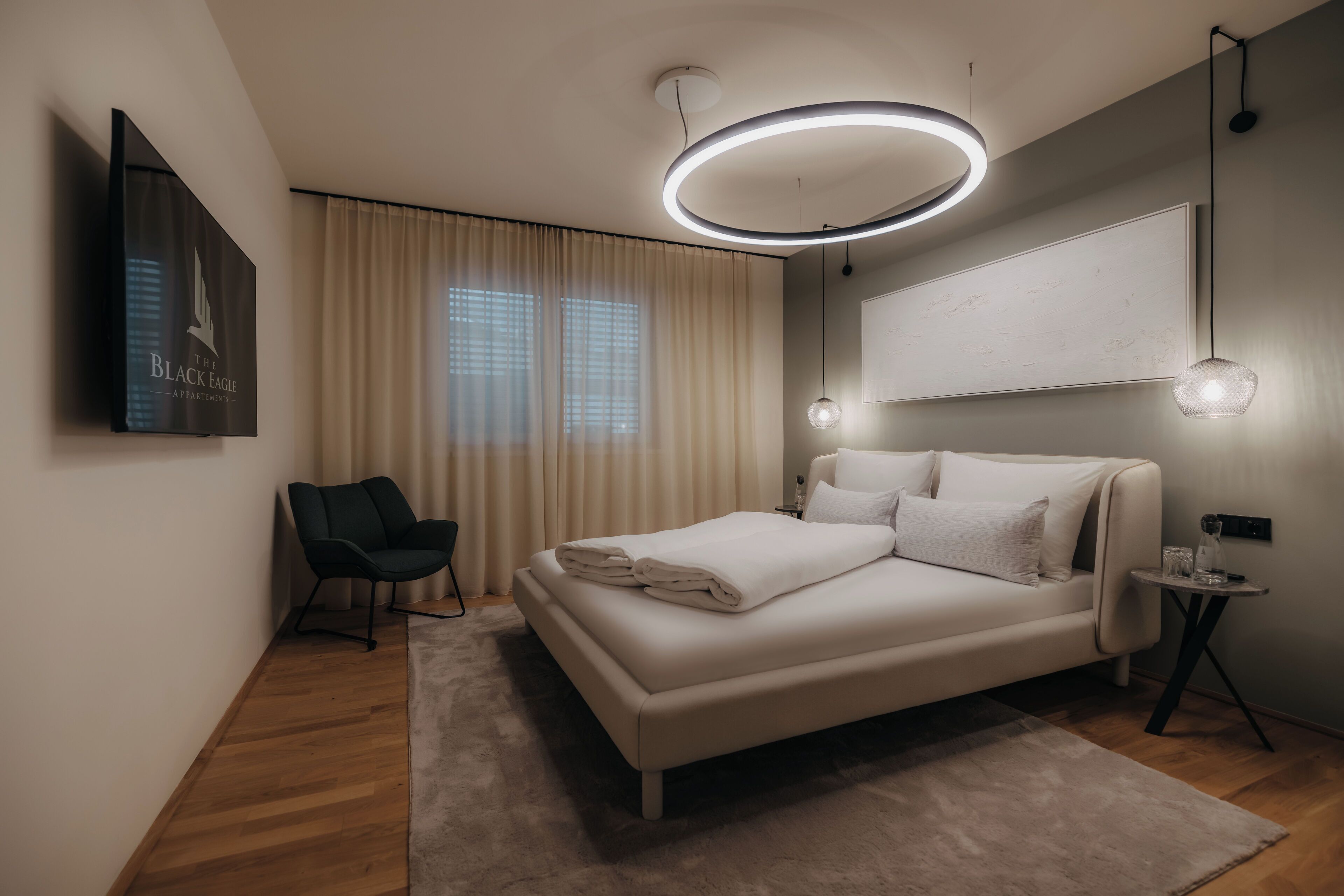 A modern bedroom with a bed, a chair, a bedside table, and a wall-mounted TV.
