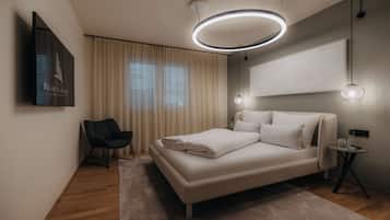 A modern bedroom with a bed, a chair, a bedside table, and a wall-mounted TV.