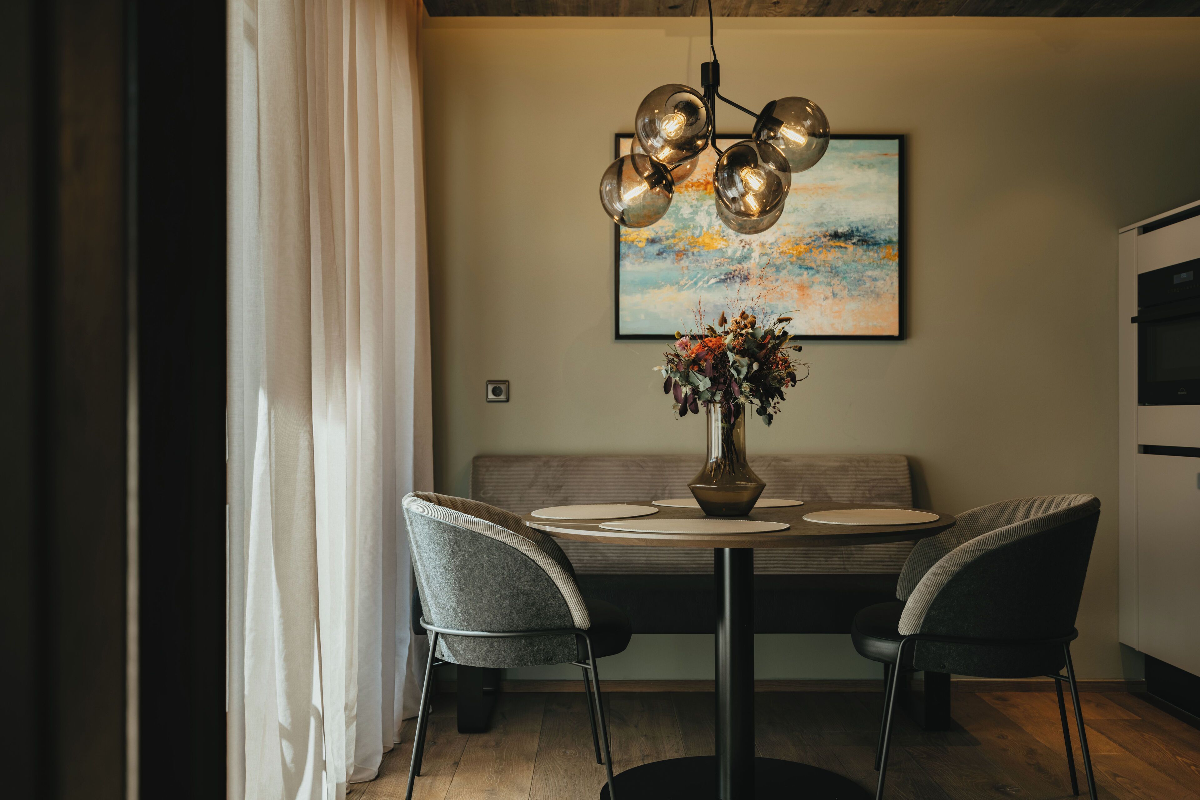 A dining area with a round table, two chairs, a vase with flowers, and a painting on the wall.