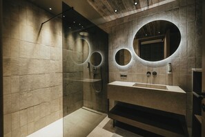 Un baño moderno con ducha envuelta en vidrio, un espejo grande y un tocador con lavamanos.