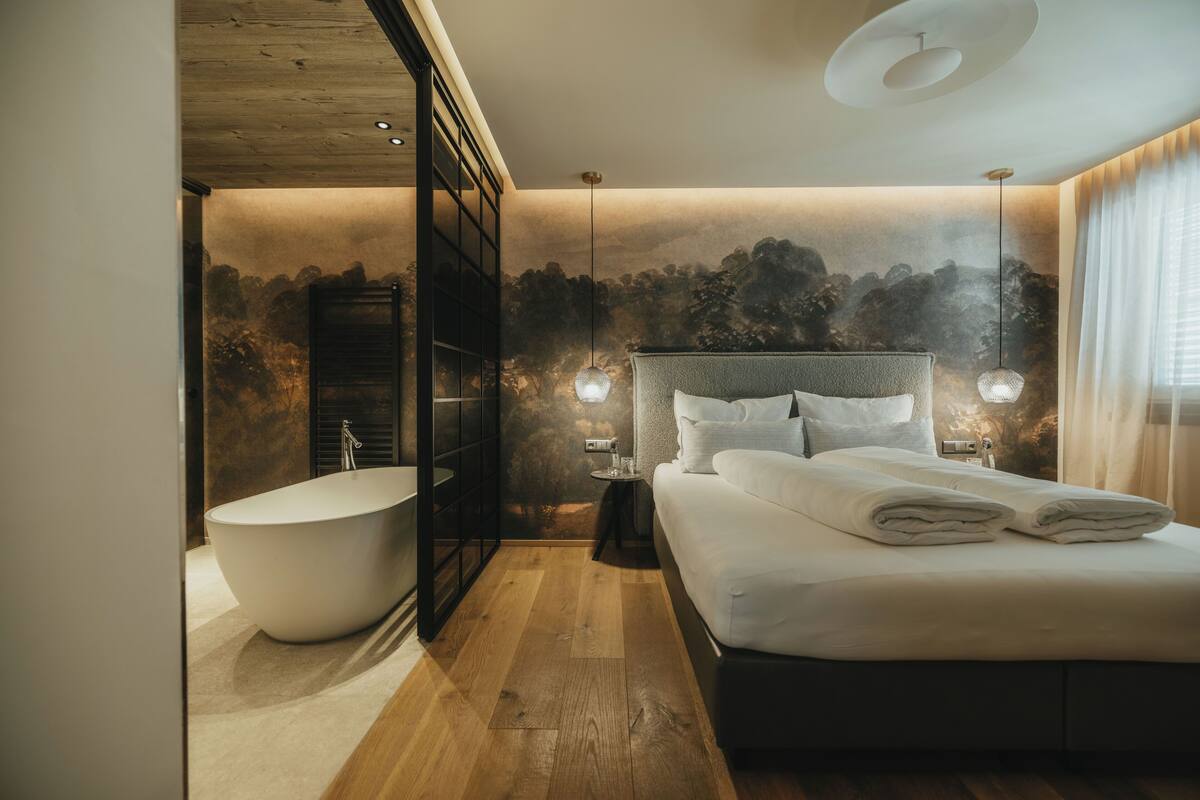 Un dormitorio moderno con una cama grande, una bañera independiente y una mesita de noche con una lámpara.