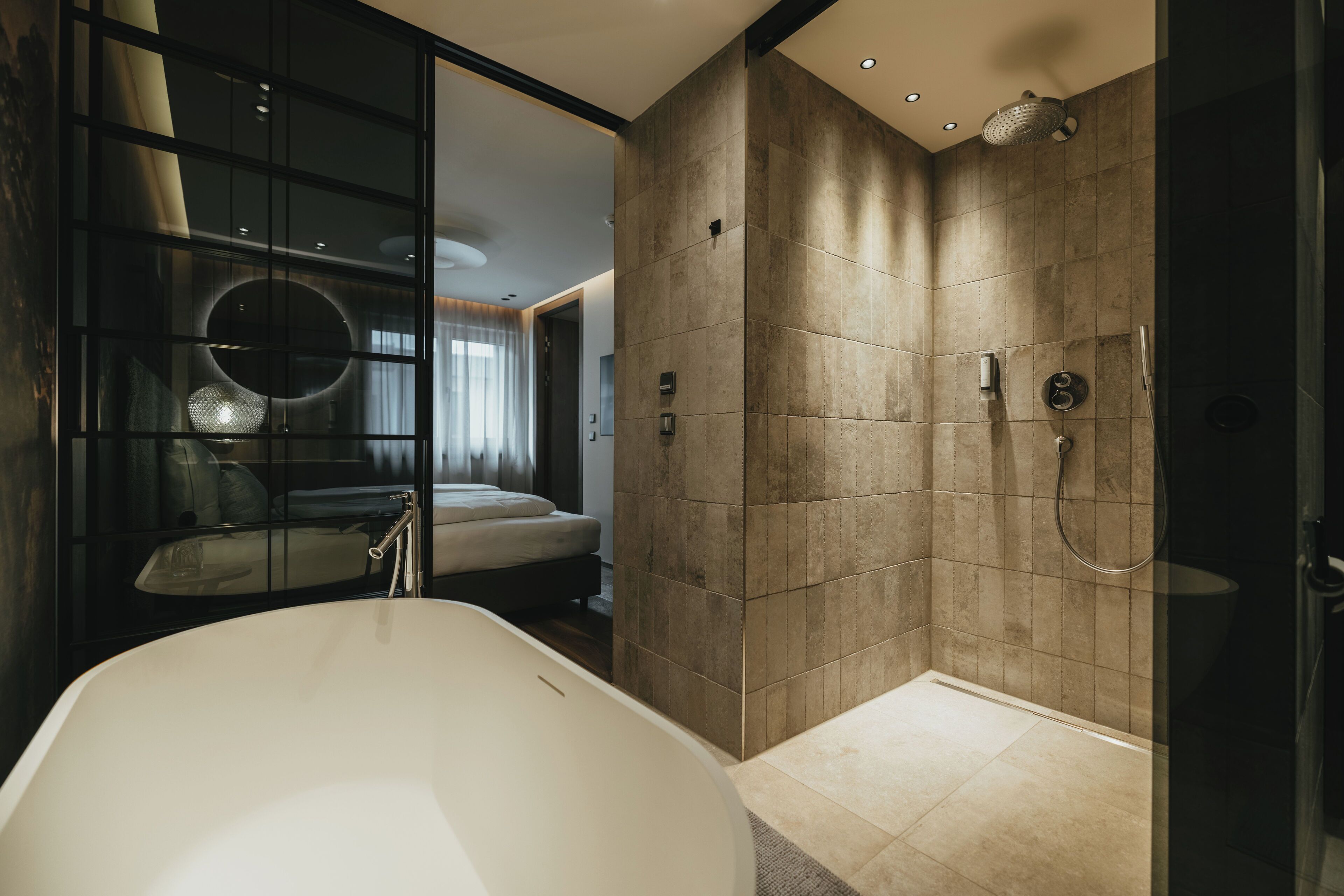A modern bathroom with a freestanding bathtub, a walk-in shower, and a glass-enclosed bedroom area.