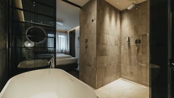 A modern bathroom with a freestanding bathtub, a walk-in shower, and a glass-enclosed bedroom area.