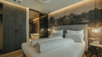 Ein modernes Schlafzimmer mit einem großen Bett, Holzboden, einem Wandpaneel als Kopfteil und einem kleinen runden Tisch mit Lampe.