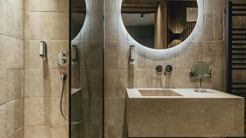 Ein modernes Badezimmer mit einer Glaskabine zur Dusche, einem großen Waschbecken mit rundem Spiegel und einer hölzernen Sitzbank.