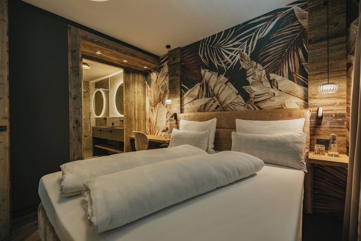 Un dormitorio con una cama grande, cabecero de madera y un mural de hojas en la pared.