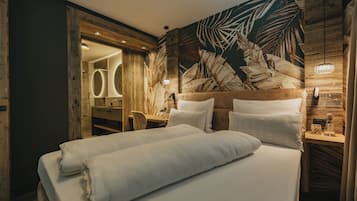 A bedroom with a large bed, wooden headboard, and a wall mural of leaves.