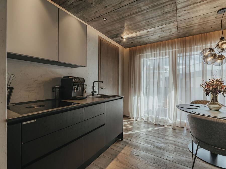 A modern kitchen with a dark countertop, a coffee machine, and a dining area with a table and chairs.