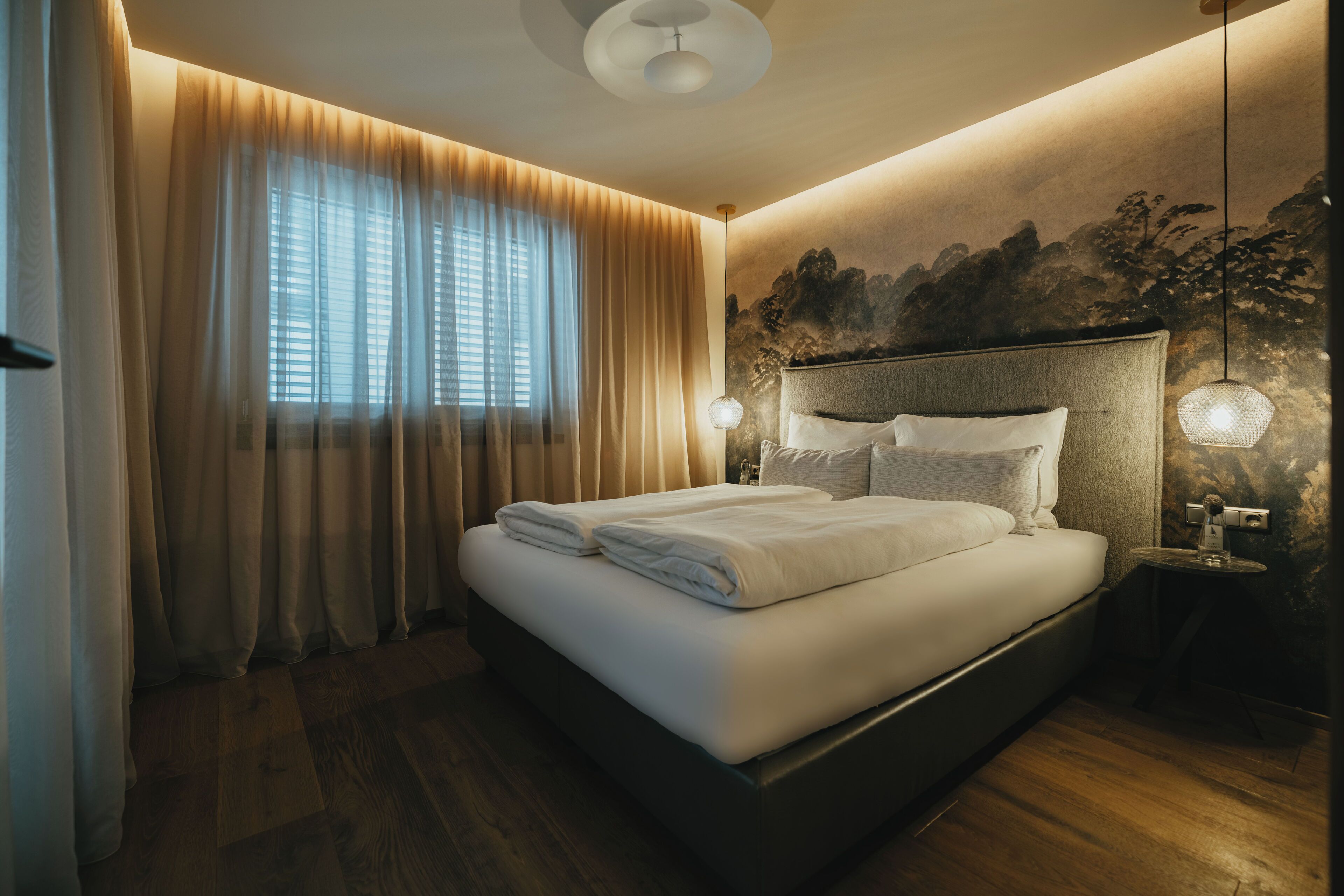 A modern bedroom with a large bed, wooden flooring, and a mural on the wall.