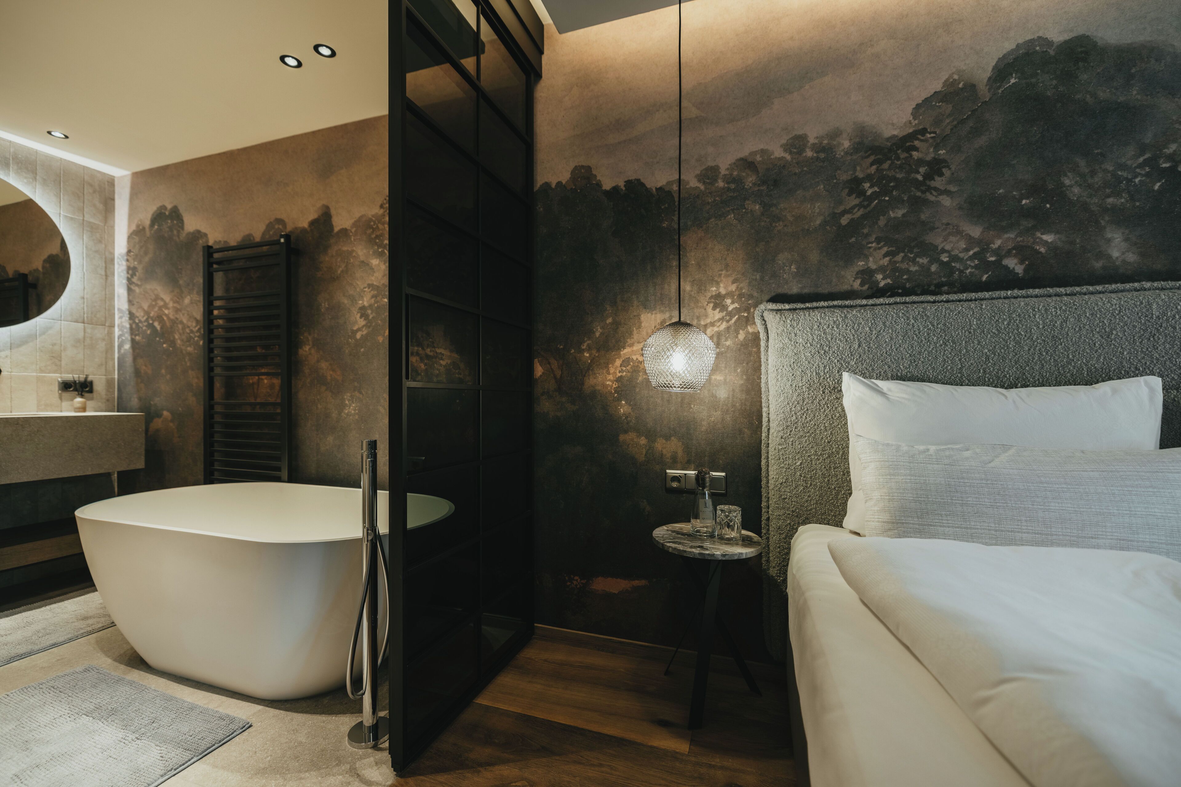 A modern bathroom with a freestanding bathtub, a round mirror, and a small table with a glass.