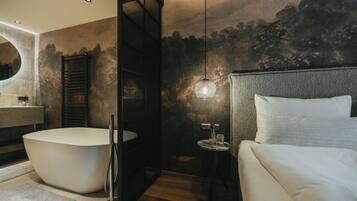 A modern bathroom with a freestanding bathtub, a round mirror, and a small table with a glass.