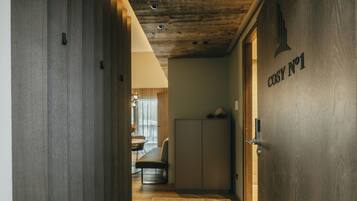 Un couloir avec une porte en bois portant l’inscription « COSY No 1 », un coin cuisine et un espace repas avec une table et des chaises.